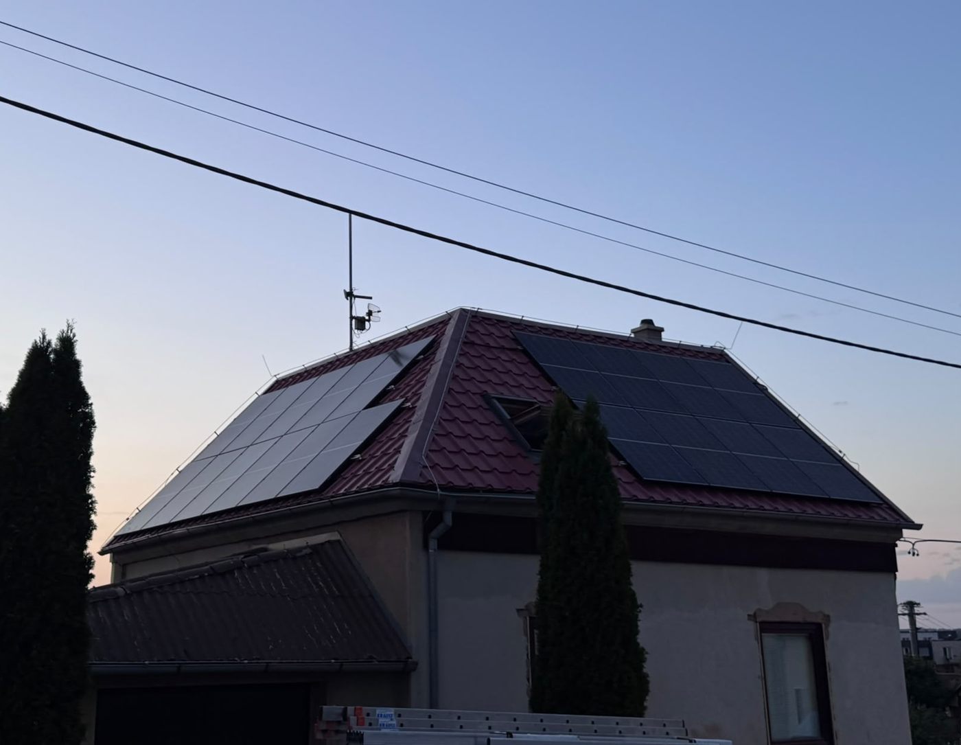 Rodinný dům s černými panely na dvou stranách valbové střechy za soumraku