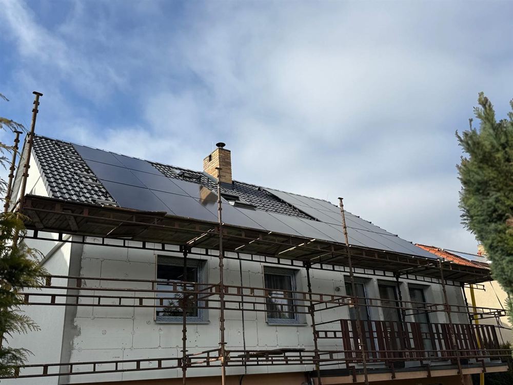 Rodinný dům s černými panely na tmavé taškové střeše, kolem domu lešení kvůli zateplení