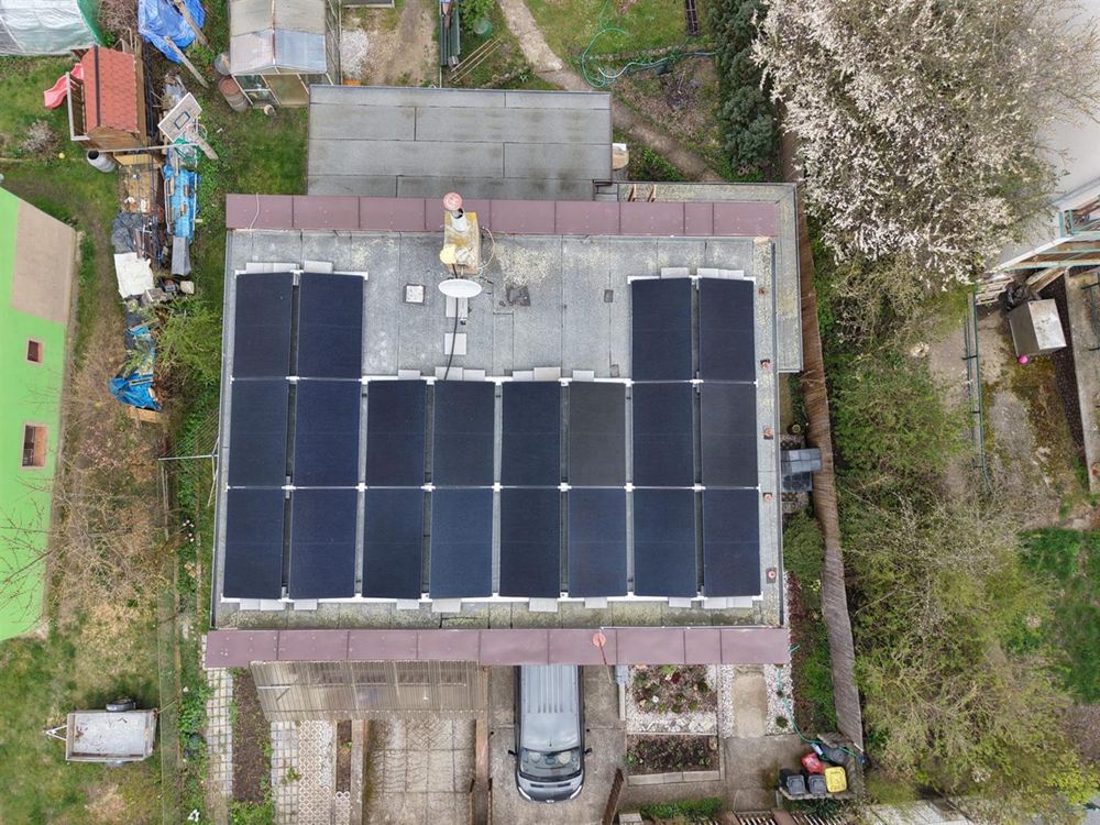 Pohled z dronu na plochou střechu rodinného domu s řadami černých panelů