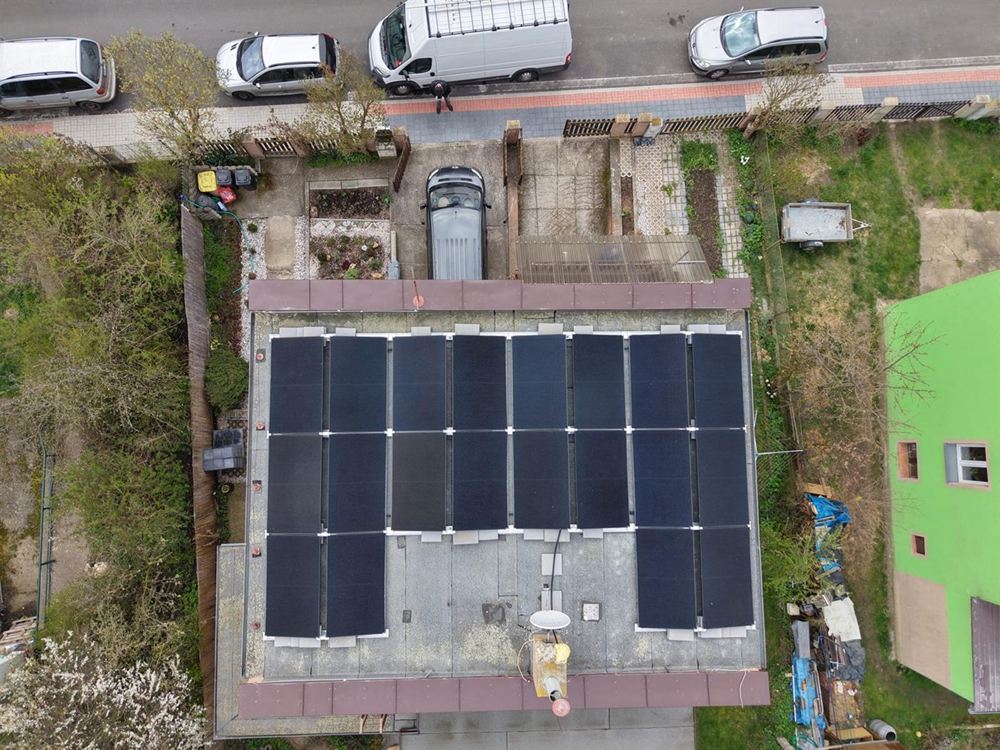 Pohled z dronu na plochou střechu s černými panely, v pozadí ulice