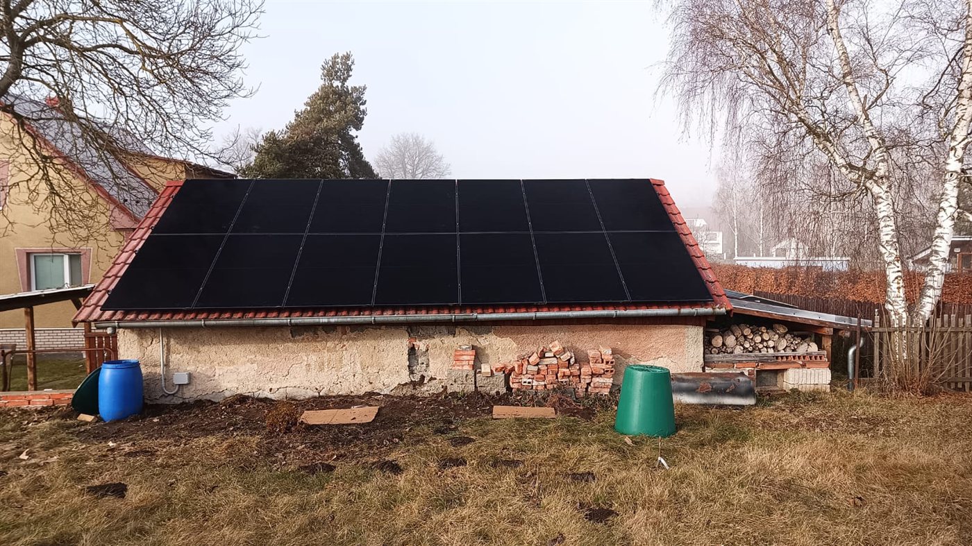 Černé panely na sedlové střeše hospodářské budovy, v zimě