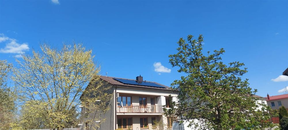 Rodinný dům s balkony a panely na střeše mezi stromy