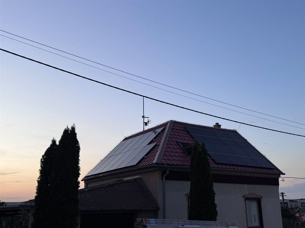 Rodinný dům s panely na dvou stranách valbové střechy za soumraku