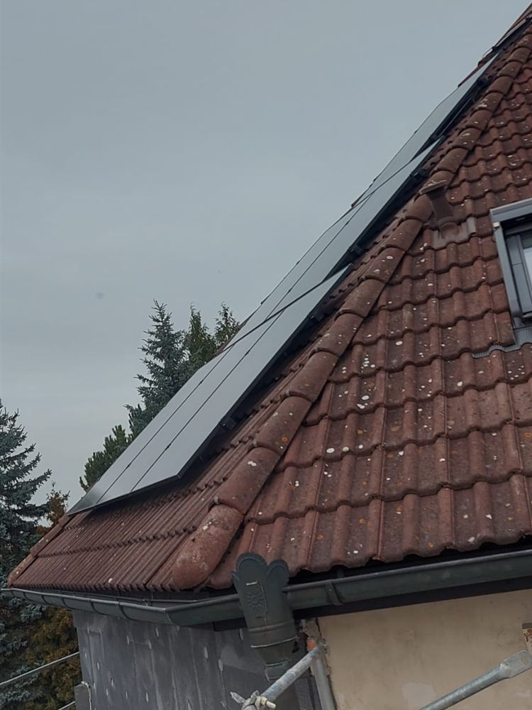 Detail valbové taškové střechy s černými panely při dokončování fasády