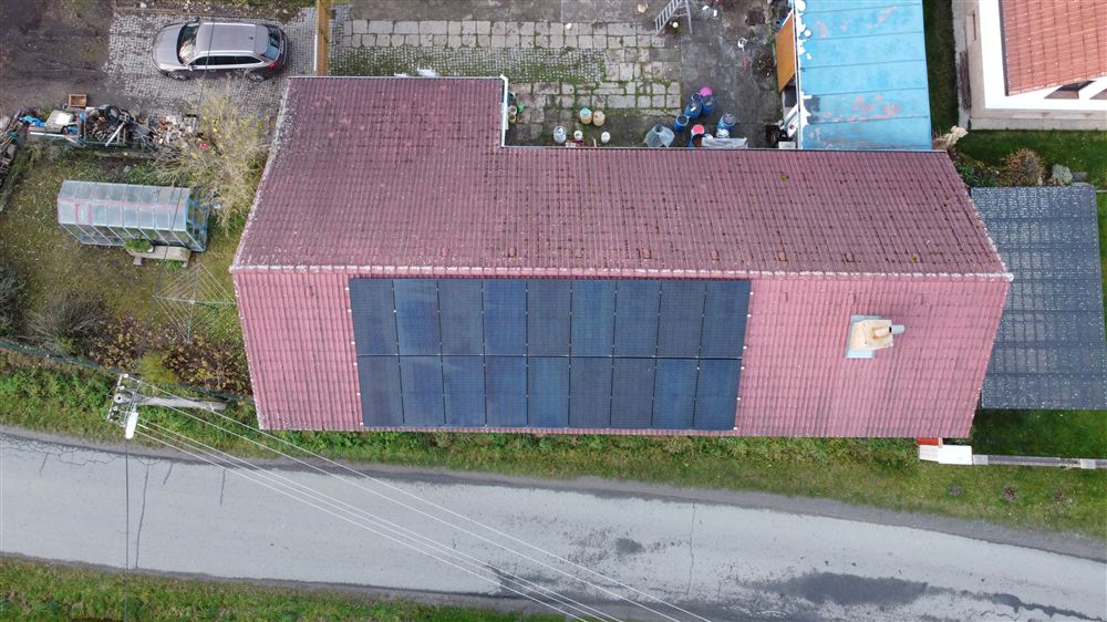 Pohled z dronu na červenou střechu rodinného domu s řadou černých panelů