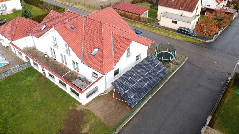 Panely na zemní konstrukci u domu s červenou střechou, pohled z dronu