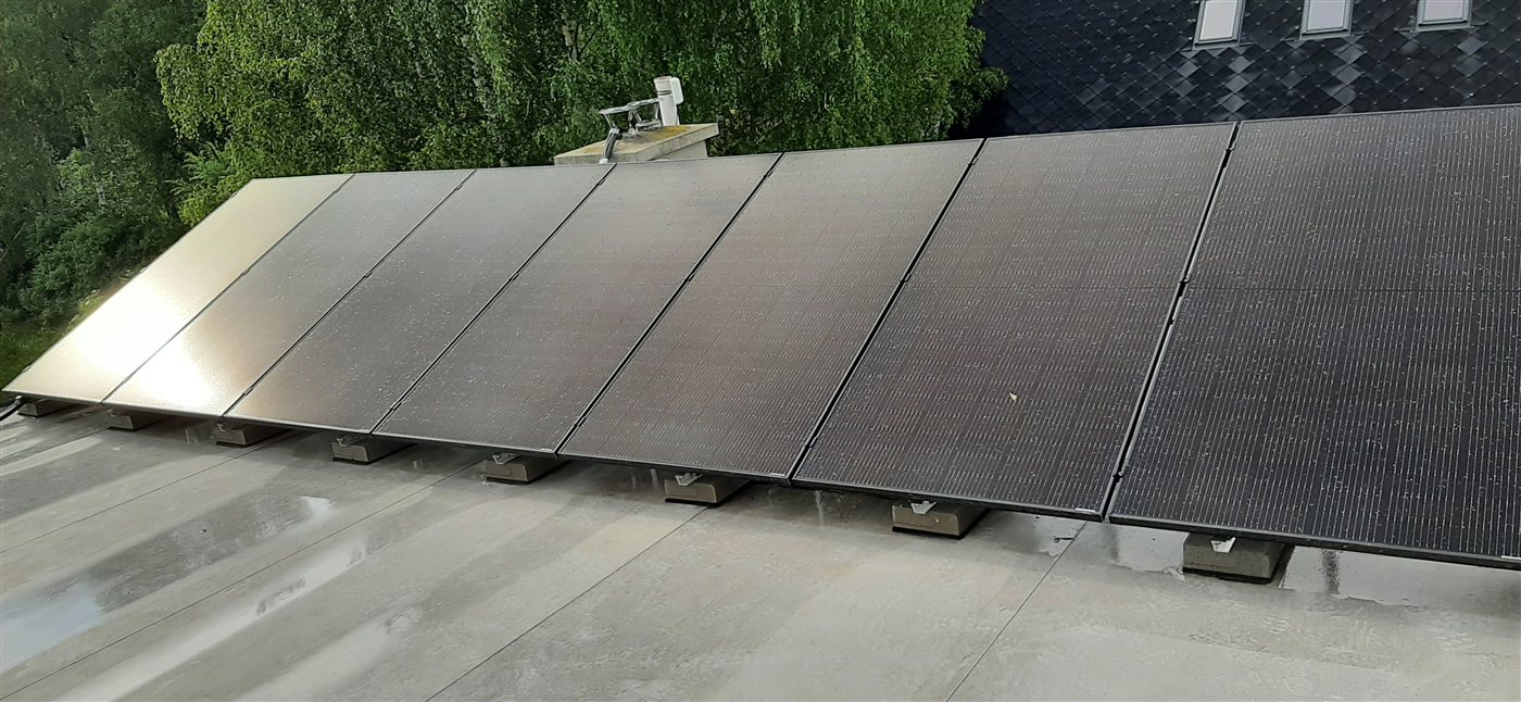 Řada černých panelů na ploché střeše na betonových patkách