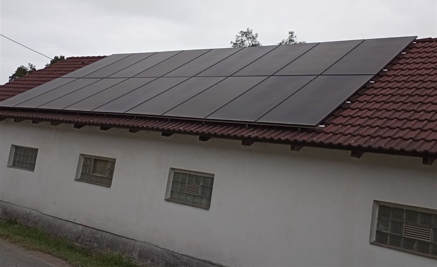 Řada černých panelů na červené taškové střeše bílé hospodářské budovy