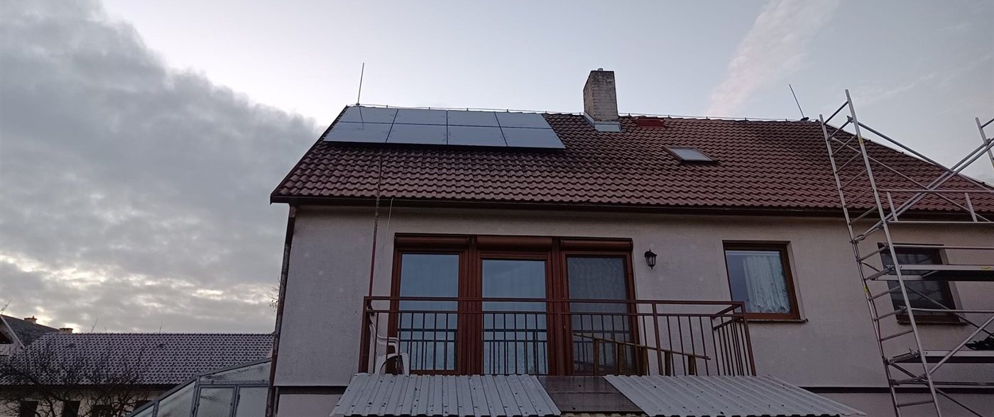 Dům s černými panely na taškové střeše za soumraku, vedle lešení