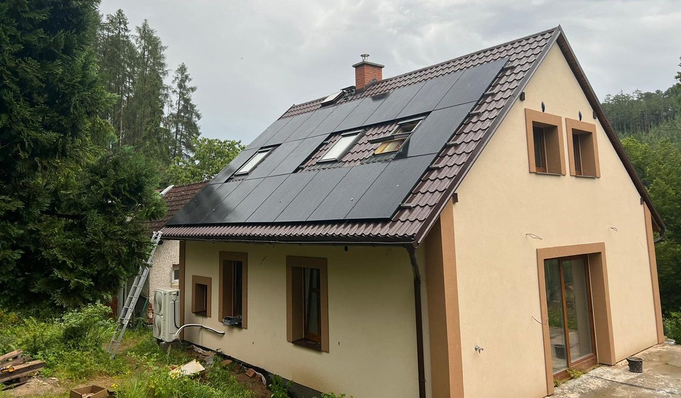 Dům s černými panely na střeše, pohled z boku mezi stromy