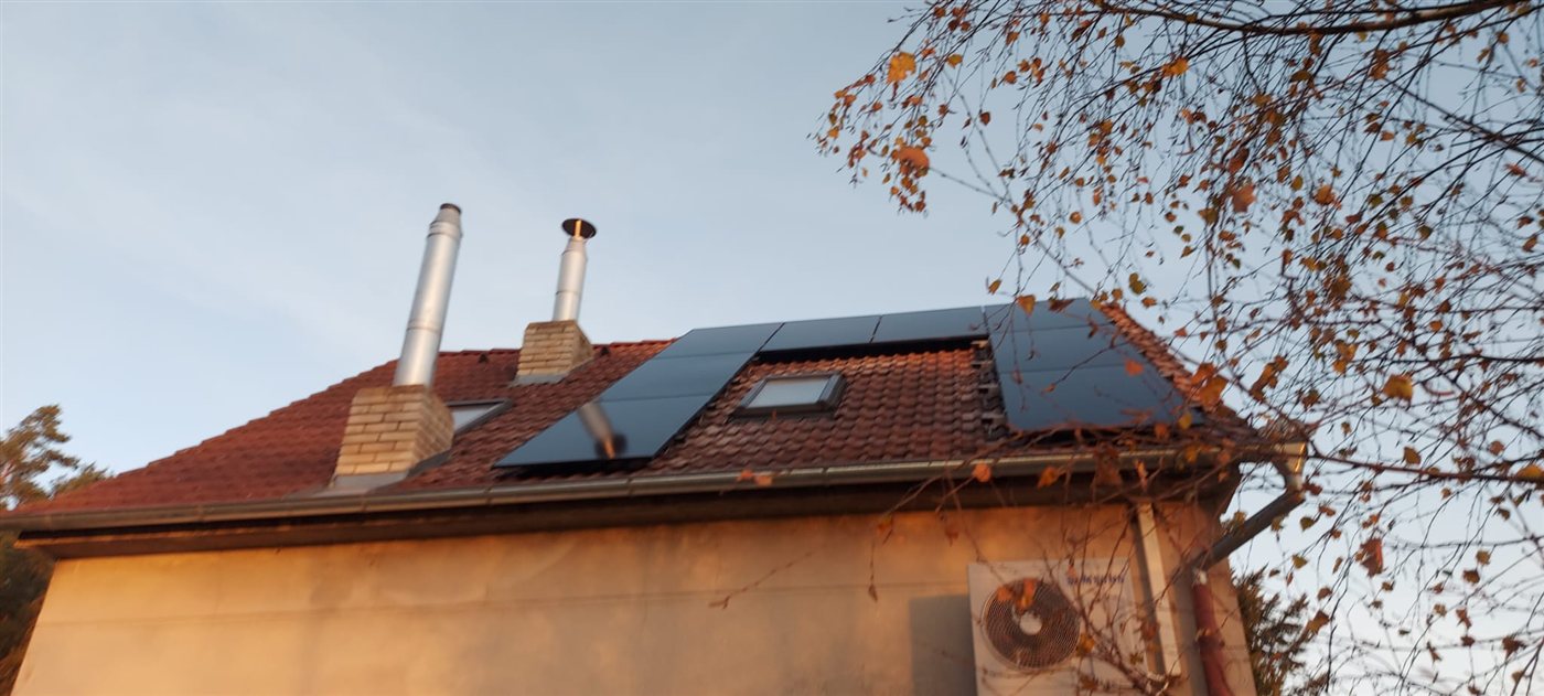 Černé panely na střeše mezi dvěma komíny, v popředí podzimní strom