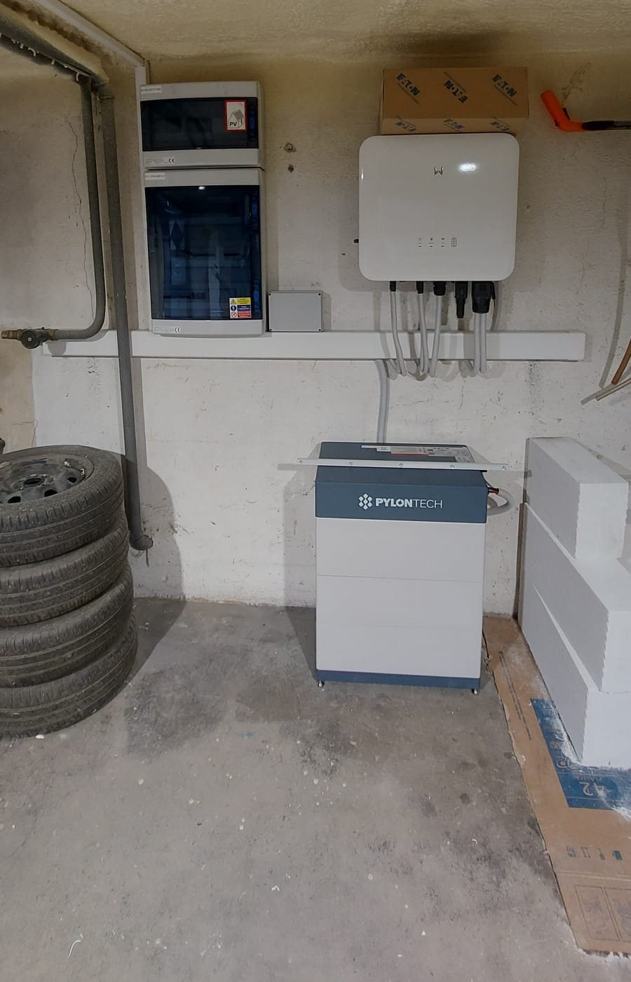 Střídač, rozvaděče a baterie Pylontech na stěně garáže