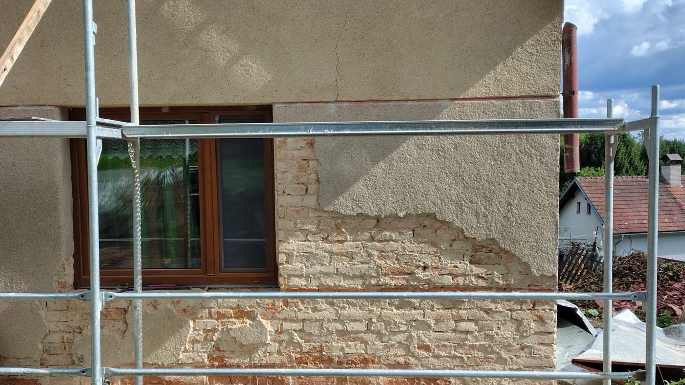 Stěna domu s otlučenou omítkou a lešením před zateplením